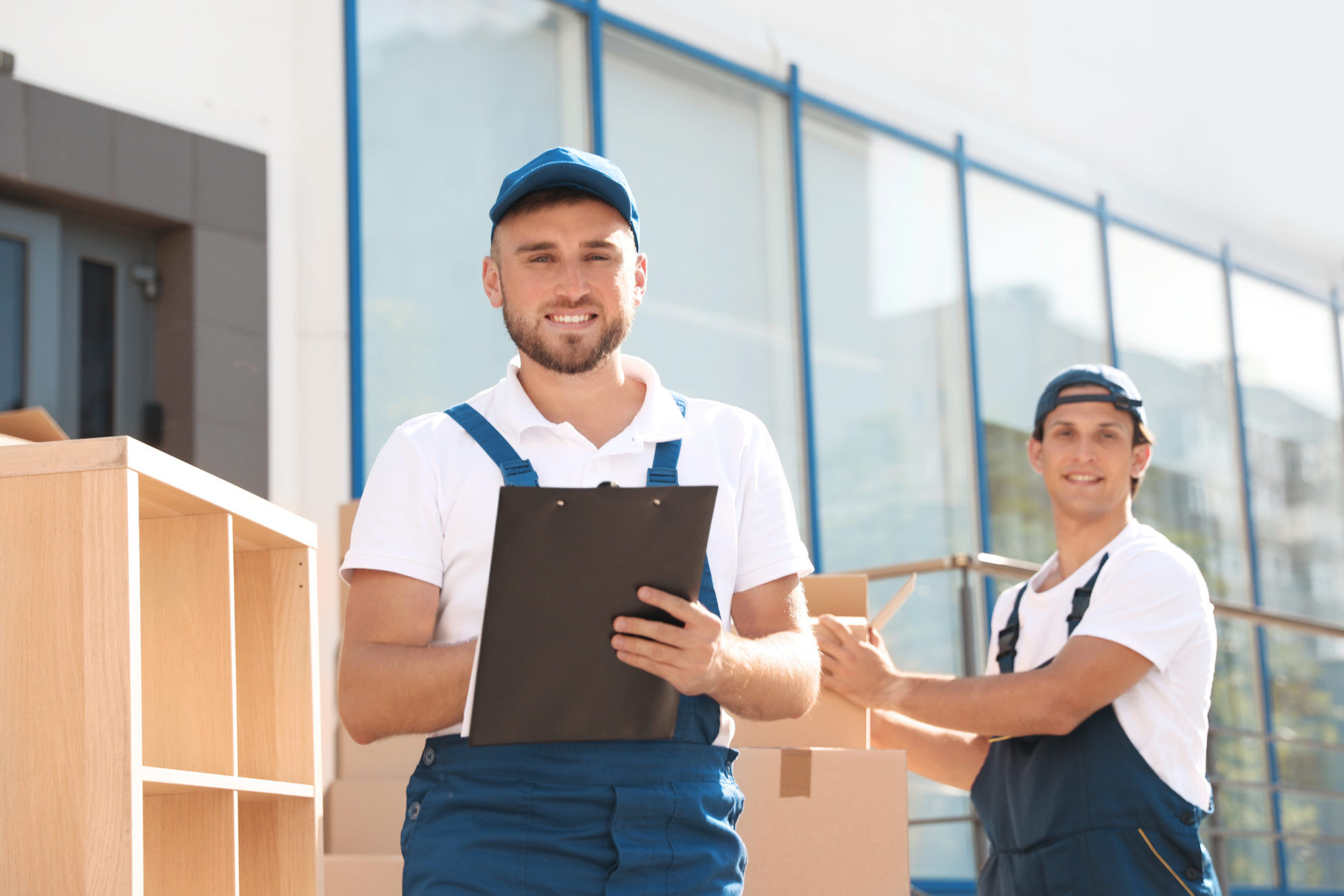 Male mover with clipboard outdoors on sunny day Packing a box with a tape gun